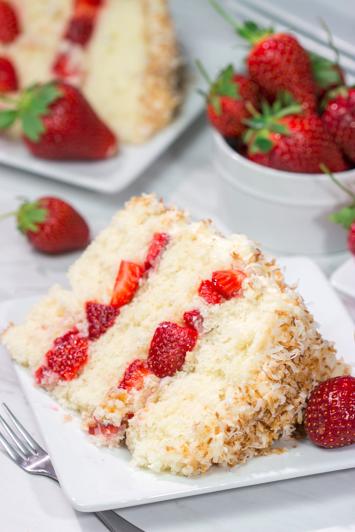 This Coconut Strawberry Cake features 3 layers of soft white cake topped with cream cheese frosting and toasted coconut. It's perfect for summer!