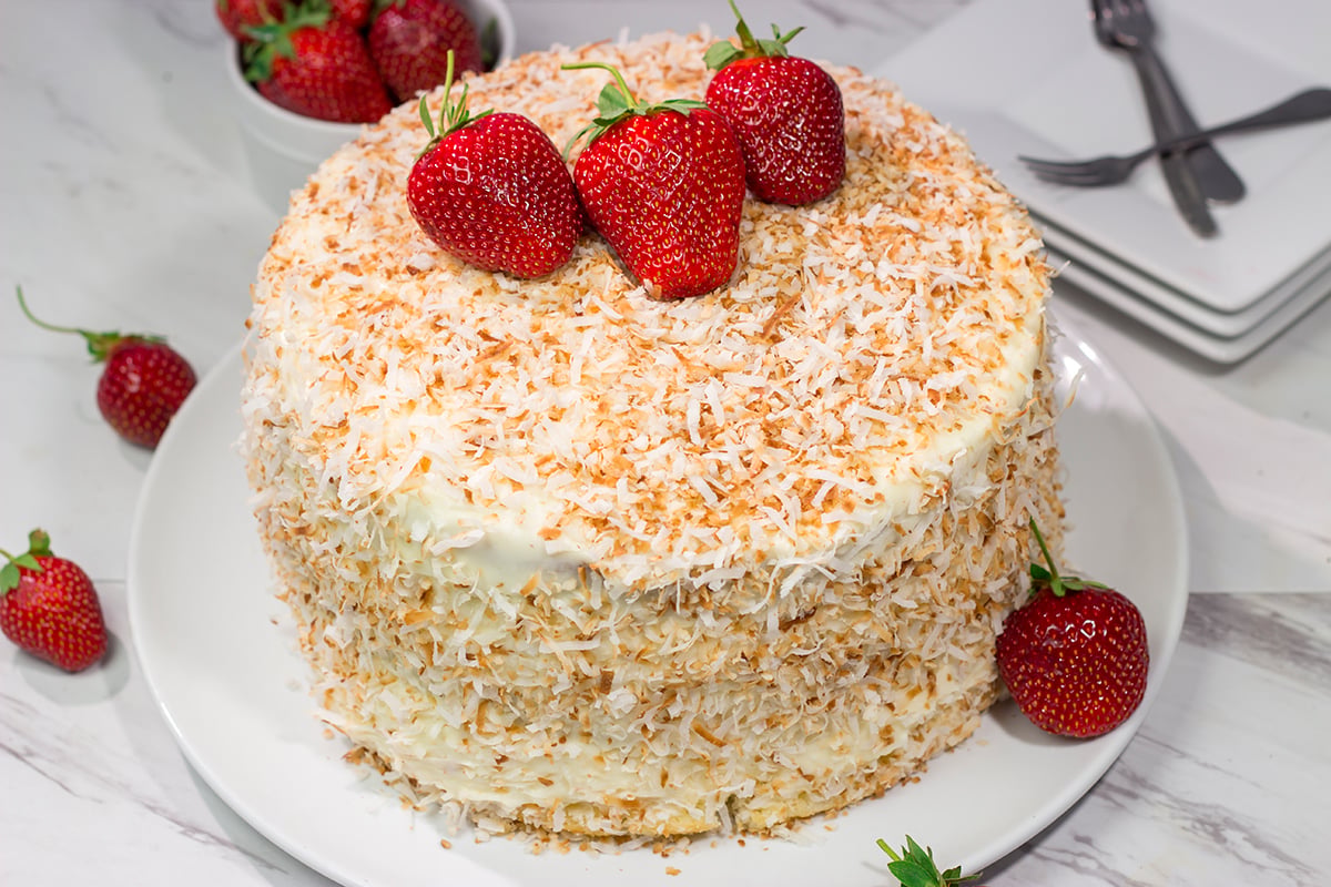 This Coconut Strawberry Cake features 3 layers of soft white cake topped with cream cheese frosting and toasted coconut. It's perfect for summer!