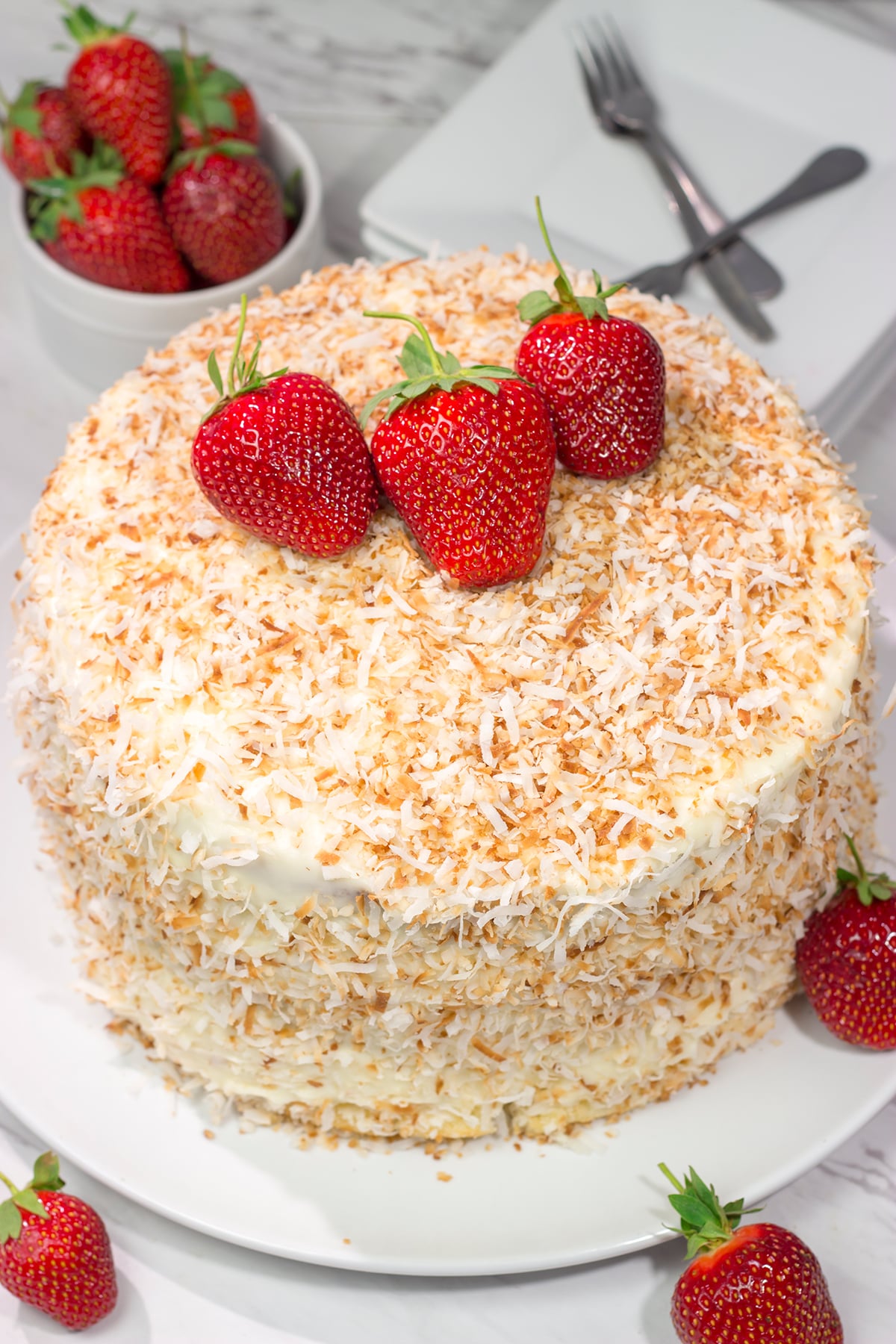 This Coconut Strawberry Cake features 3 layers of soft white cake topped with cream cheese frosting and toasted coconut. It's perfect for summer!