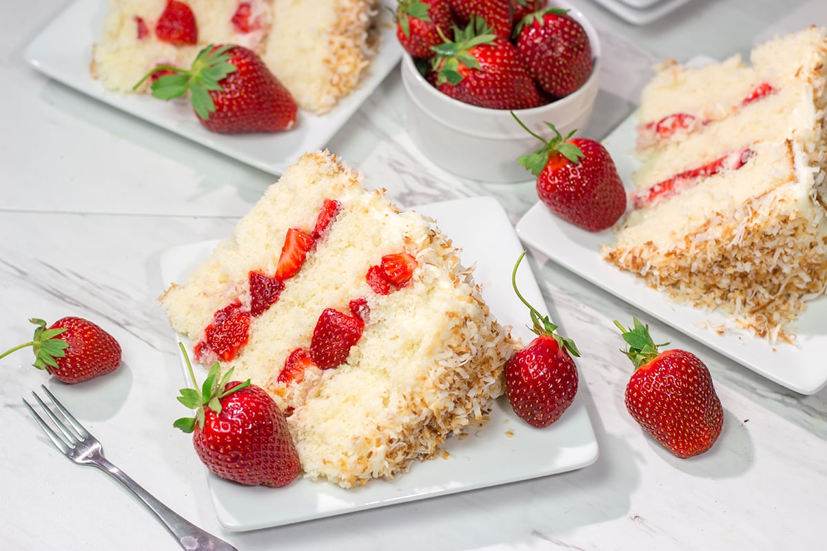 This Coconut Strawberry Cake features 3 layers of soft white cake topped with cream cheese frosting and toasted coconut. It's perfect for summer!