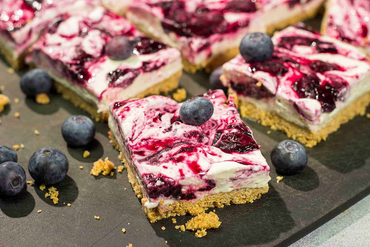 These No Bake Blueberry Cheesecake Bars feature a creamy cheesecake filling swirled with fresh blueberry jam on top of a buttery graham cracker crust. They're perfect for a hot summer day!