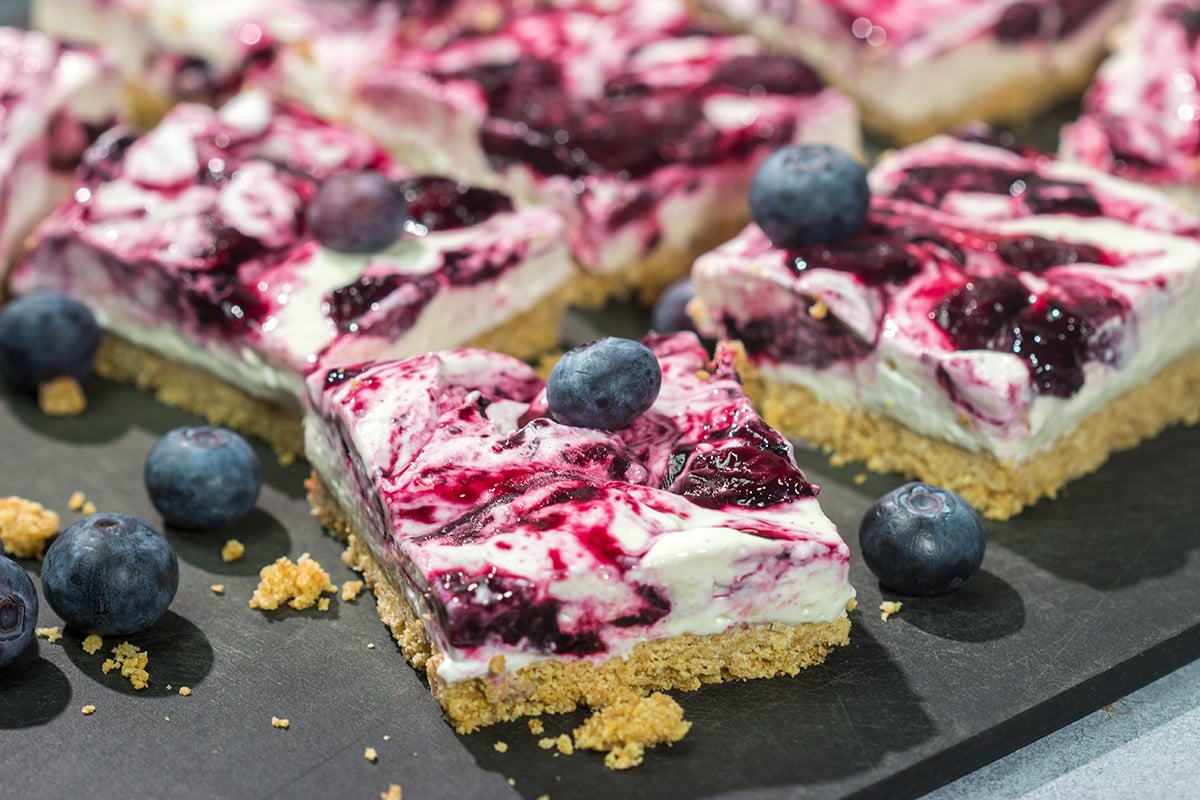 These No Bake Blueberry Cheesecake Bars feature a creamy cheesecake filling swirled with fresh blueberry jam on top of a buttery graham cracker crust. They're perfect for a hot summer day!